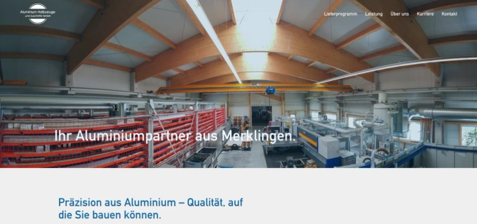 Startseite von Aluminium Halbzeuge und Zuschnitte: Blick in die Fertigungshalle mit Holzbinderdach, Kranbahn und roten Lagerregalen, darüber der Schriftzug Ihr Aluminiumpartner aus Merklingen.