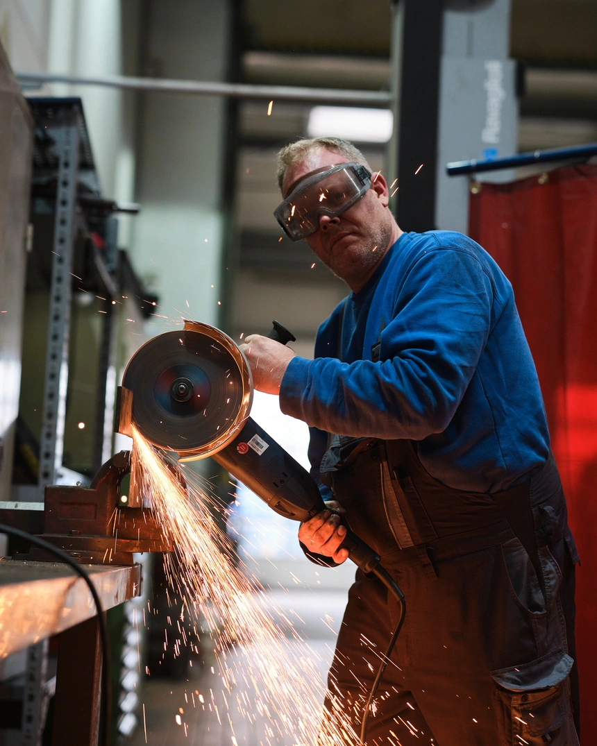 Metallbearbeiter mit Schutzbrille am Winkelschleifer, Funken sprühen