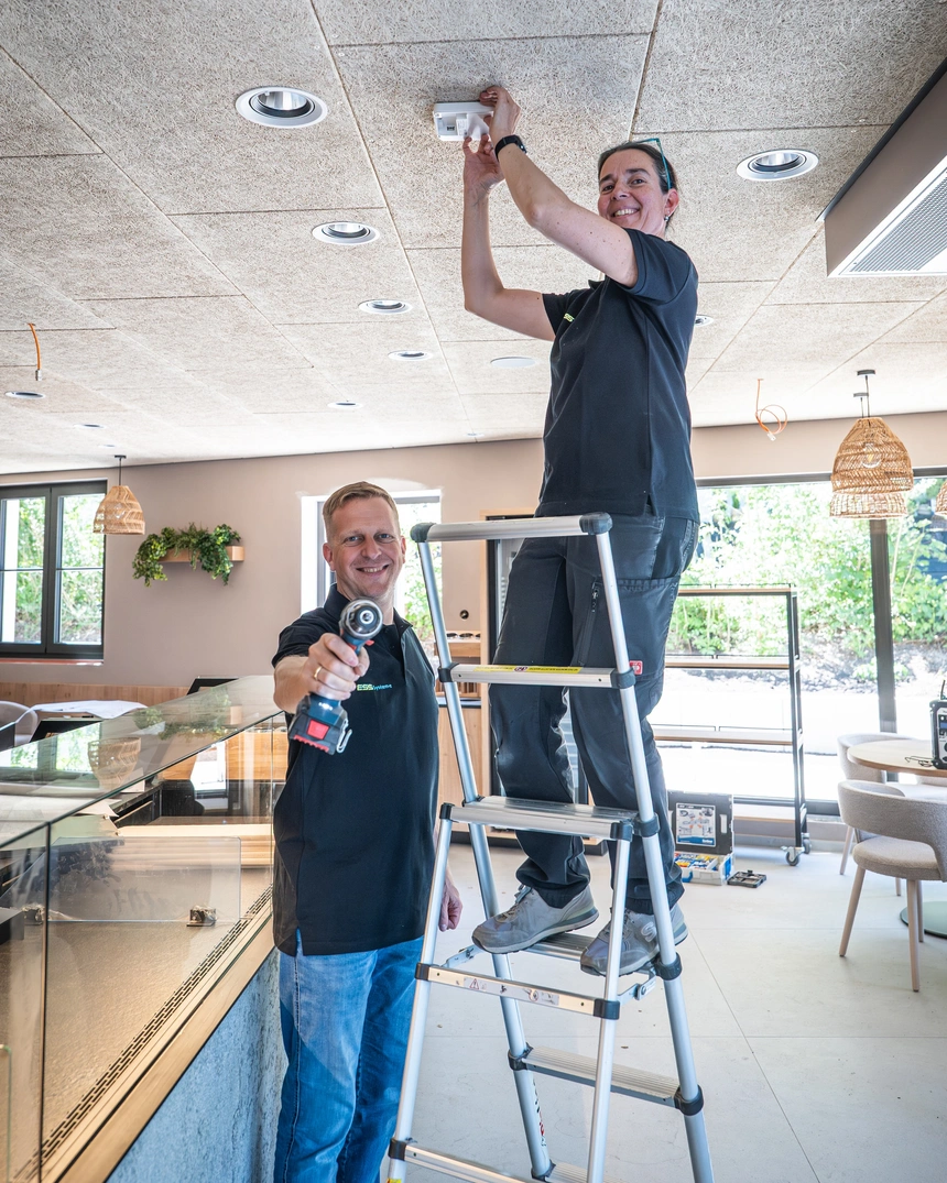 Elektriker auf der Leiter bei der Montage an der Decke, ein Kollege steht daneben