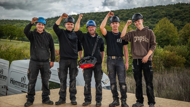 Fünf Mitarbeiter von Herrmann Holzbau mit Helmen recken auf einer Baustelle die Faust