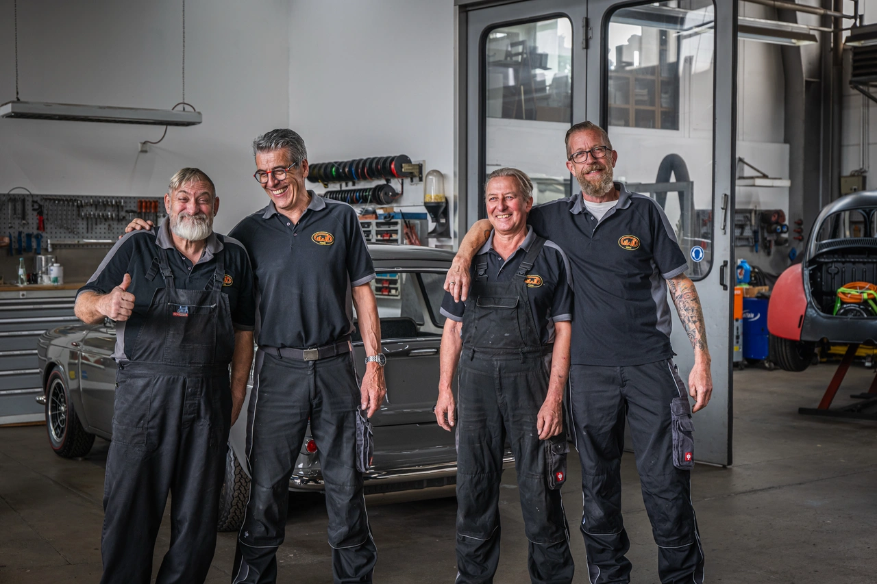 Vier Mechaniker stehen lachend Arm in Arm in ihrer Werkstatt