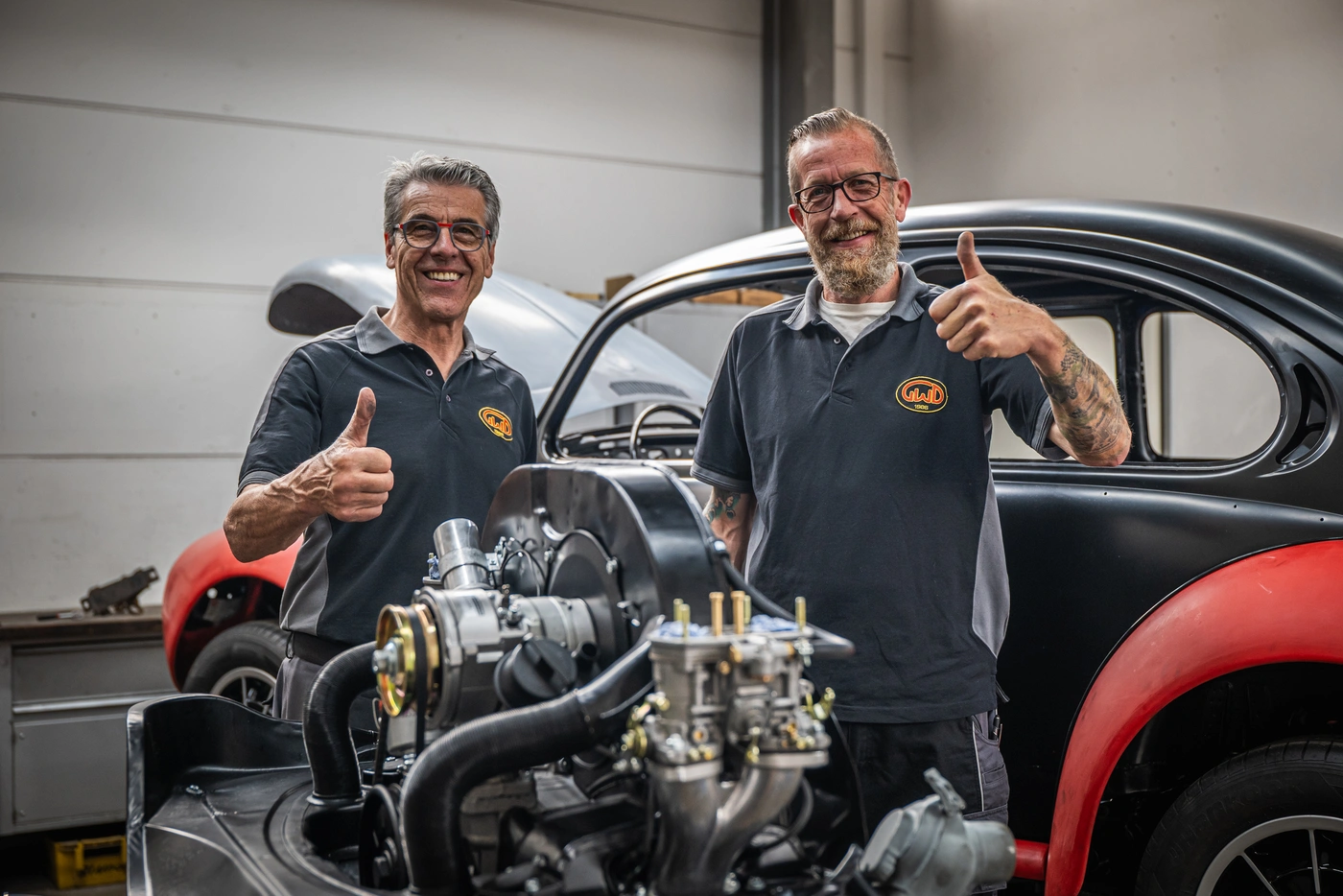 Zwei Kfz-Mechaniker neben einem ausgebauten Motor und einer Karosserie