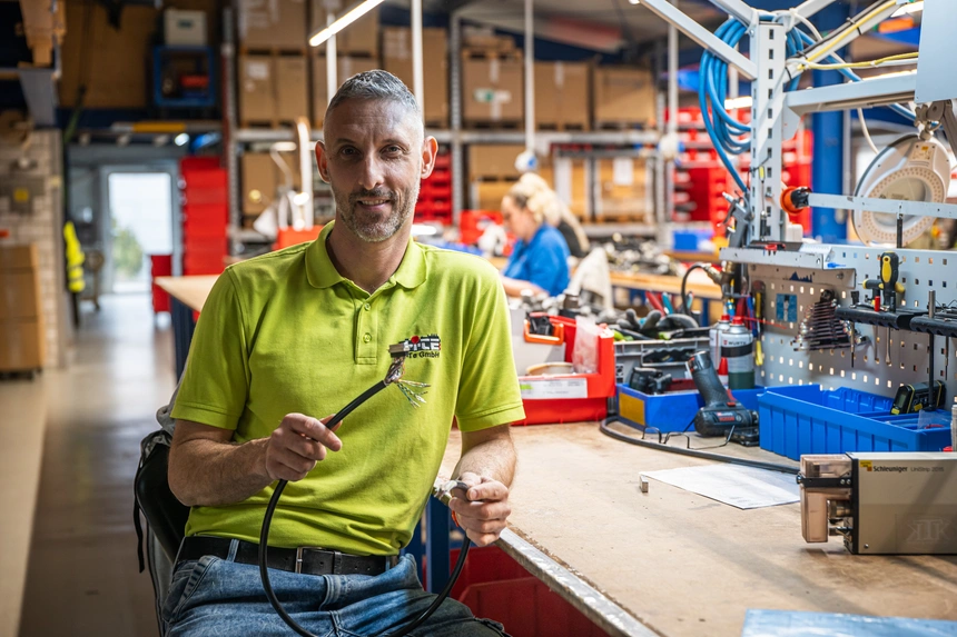 Mitarbeiter in der Fertigung an einer Montagelinie, im Hintergrund Materialkisten und Werkbänke