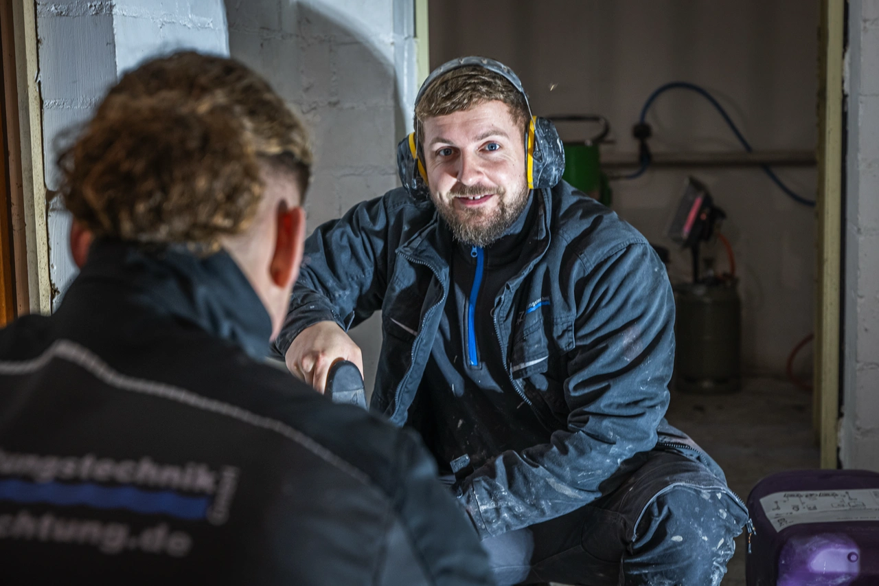 Zwei Handwerker geben sich in der Werkstatt die Hand, einer lacht in die Kamera