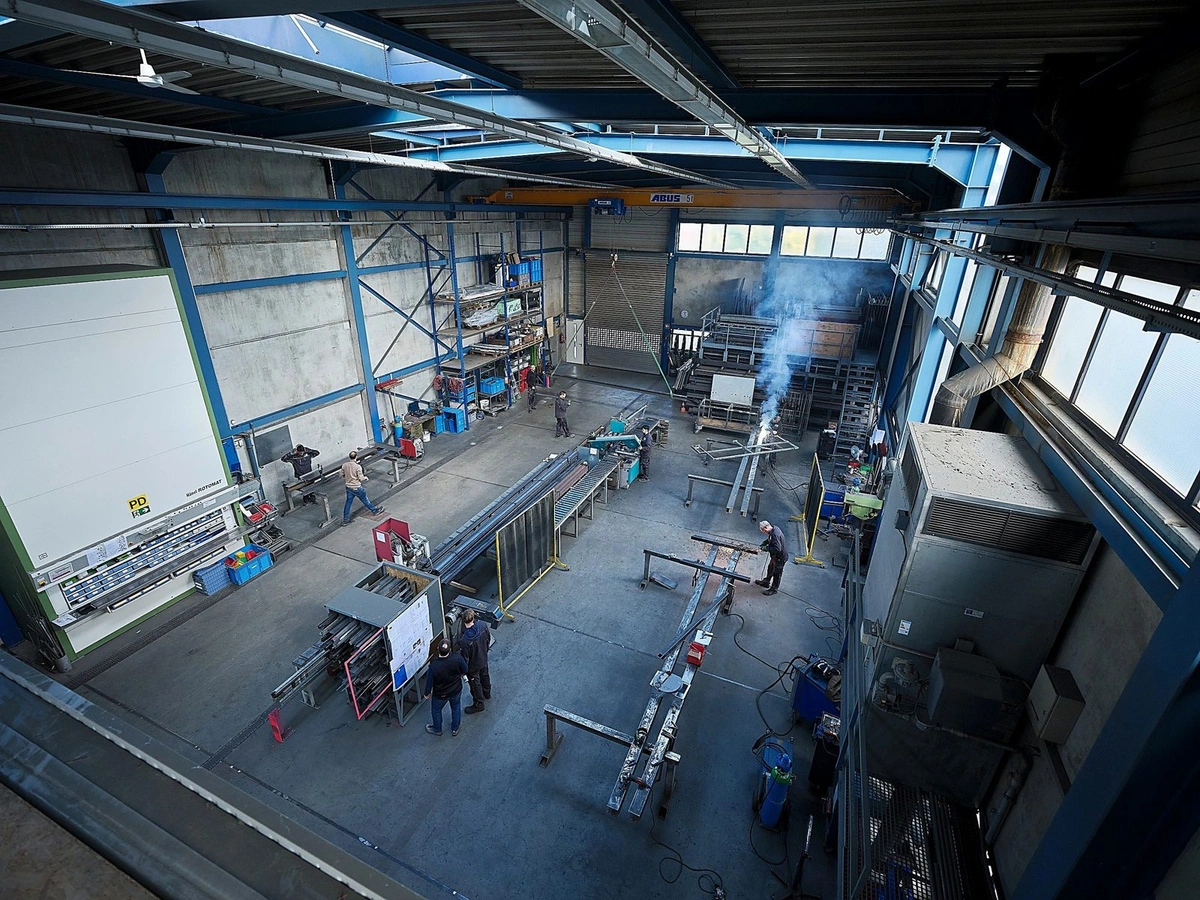 Blick von oben in eine Metallbauwerkstatt, mehrere Mitarbeiter arbeiten an langen Stahlprofilen
