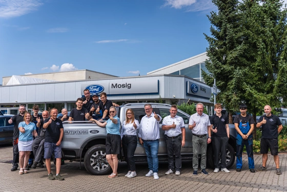 Die Belegschaft vom Autohaus MOSIG vor dem Autohaus, im Hintergrund das Ford-Schild und der Ausstellungsbau