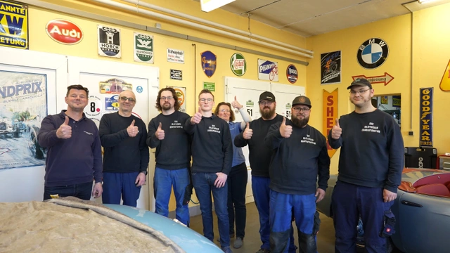 Standbild aus dem Imagefilm für Die Oldtimermanufaktur: das Team in der Werkstatt zwischen historischen Fahrzeugen und alten Emailschildern