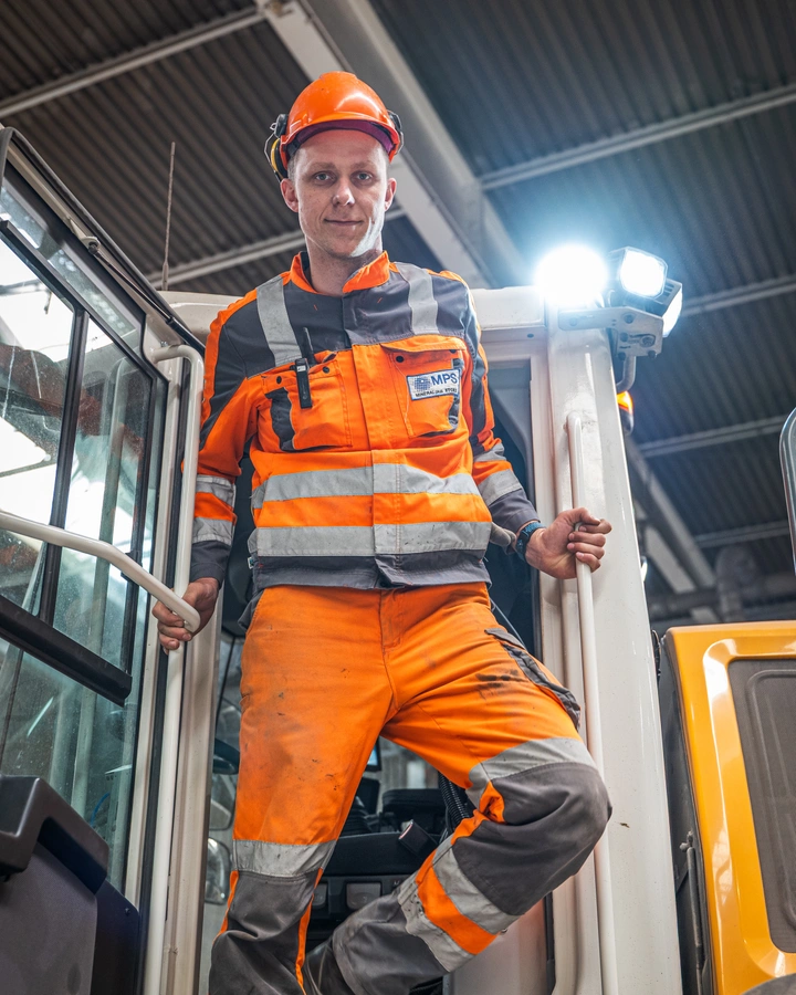 Mitarbeiter in orangefarbener Warnkleidung steigt aus der Kabine eines Radladers